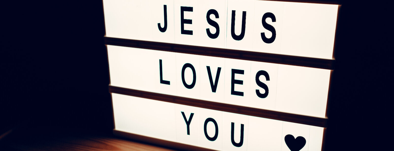 schwarze Schrift auf hellen Lichtbalken, Text: Jesus loves you; daneben ein Herz